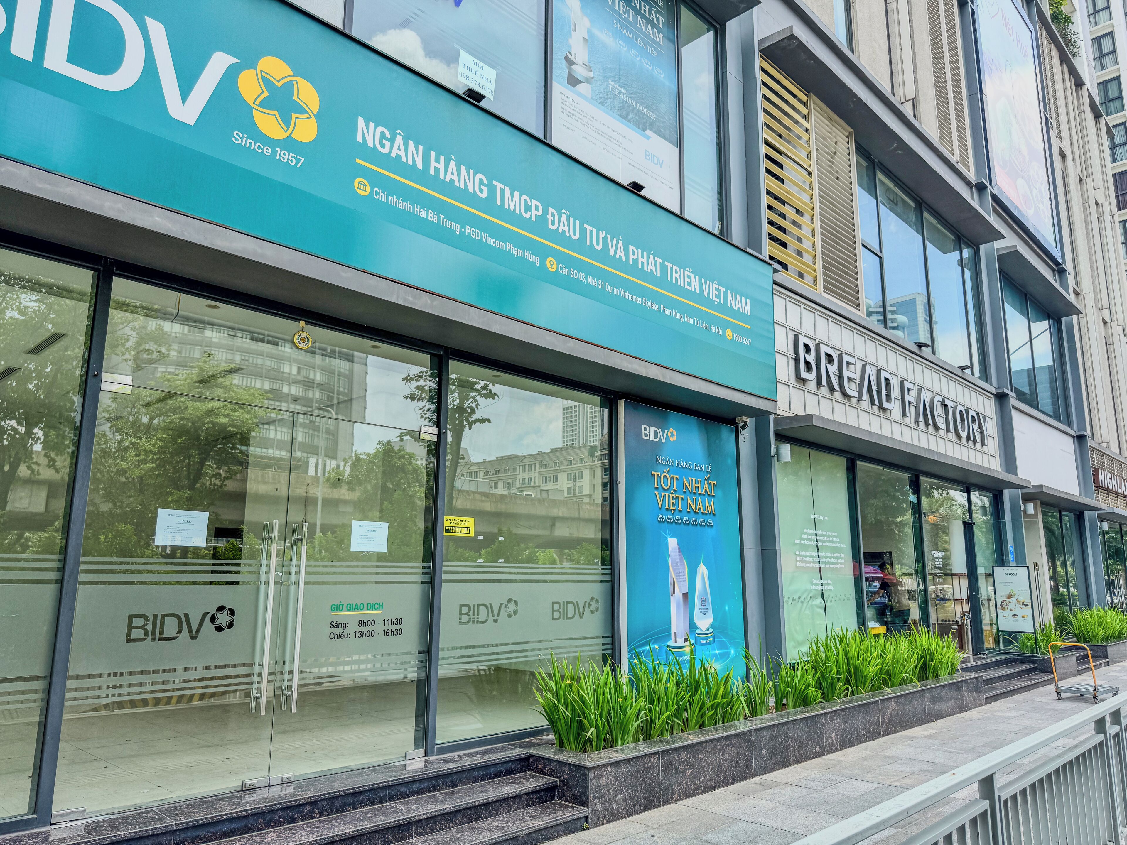 Un edificio con un gran cartel de BIDV, un escaparate moderno de vidrio y un anuncio para BREAD FACTORY.