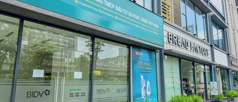 Un edificio con un gran cartel de BIDV, un escaparate moderno de vidrio y un anuncio para BREAD FACTORY.
