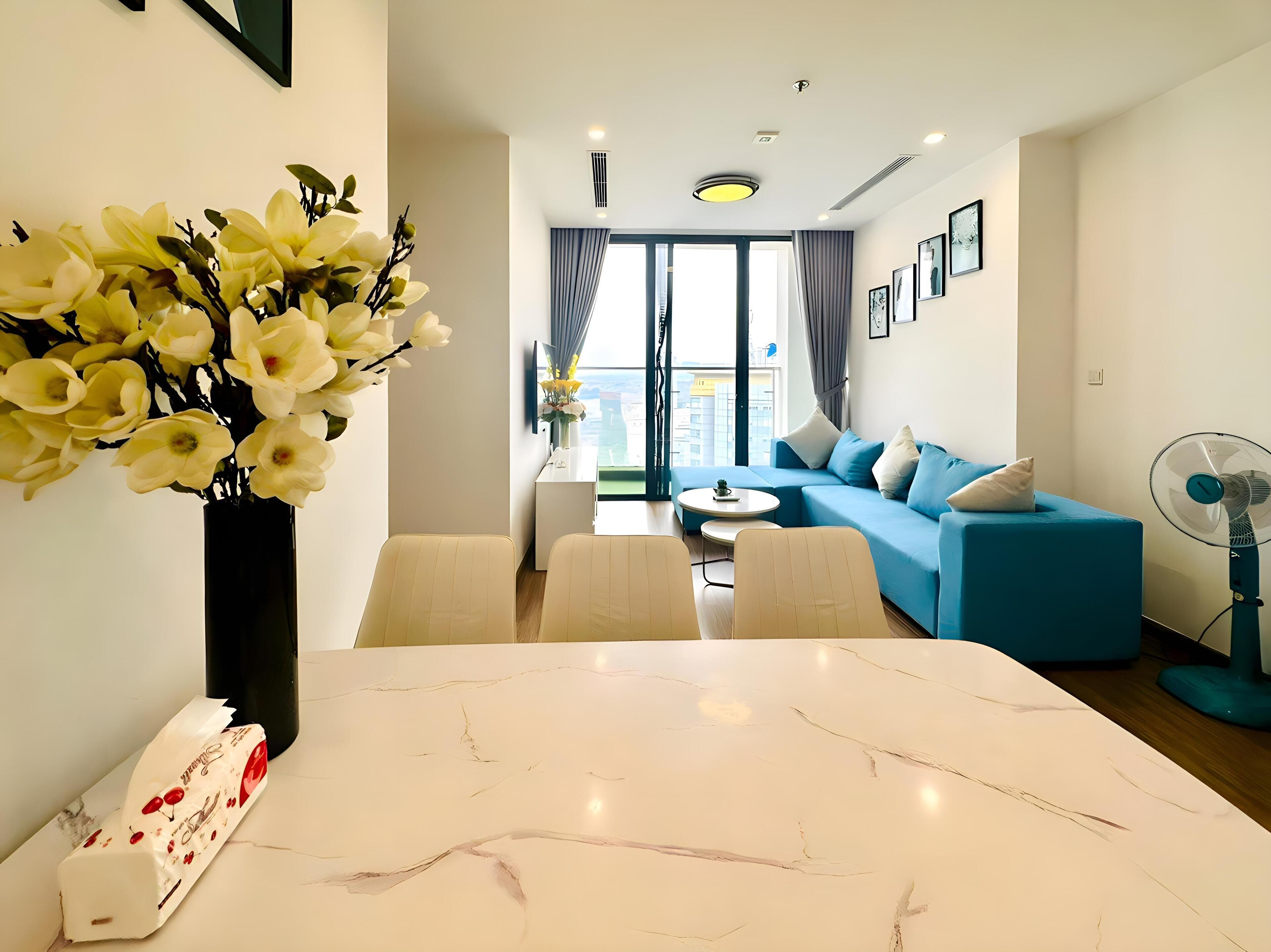 A modern living room with a blue sofa, a dining table, and a vase of flowers.