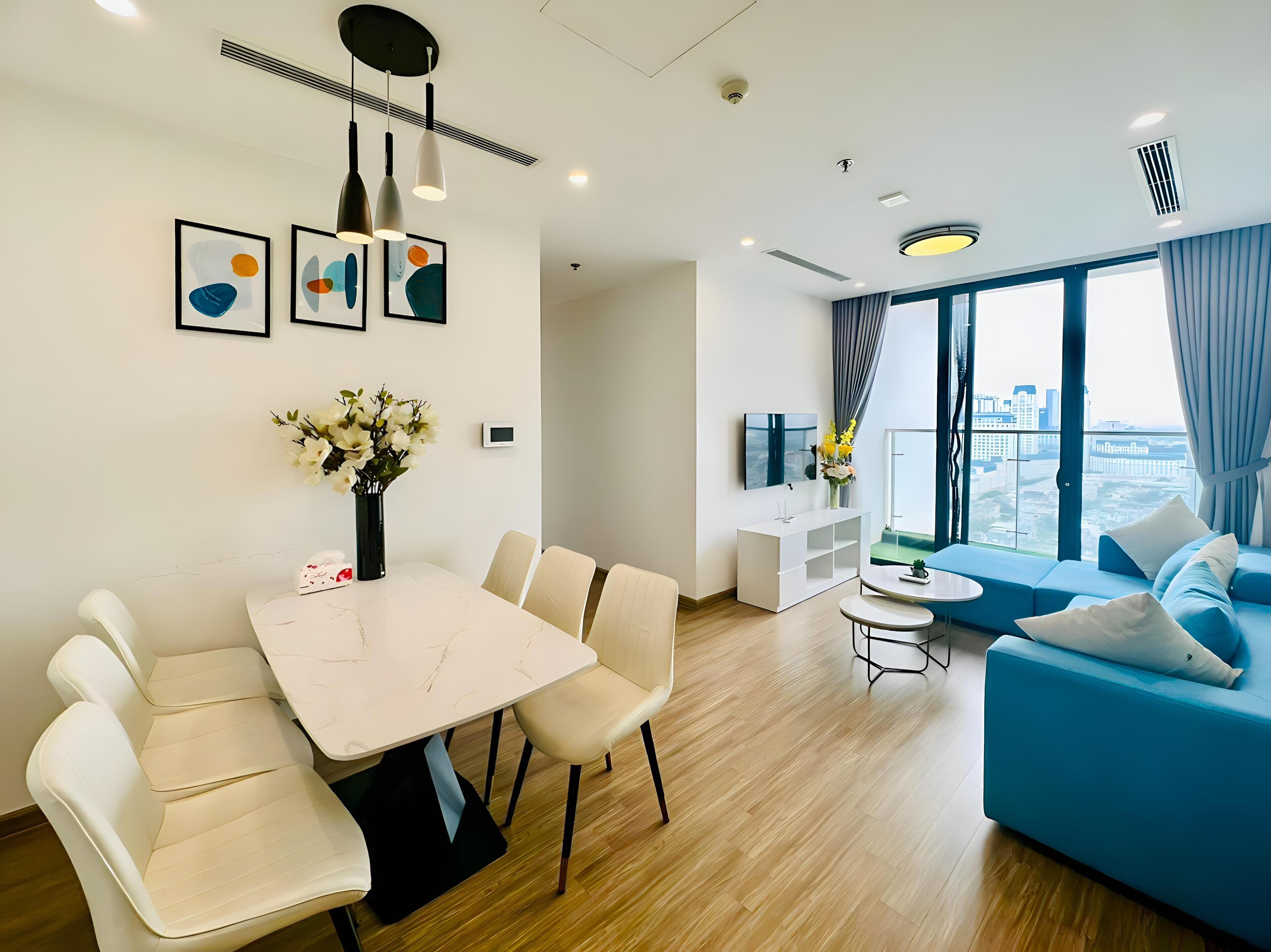 Ein modernes Wohnzimmer mit Essbereich, einem blauen Sofa und Blick auf die Stadt durch große Fenster.