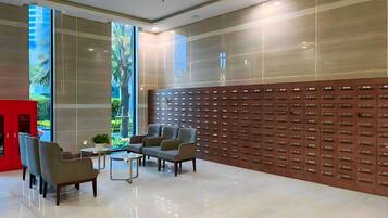 A modern lobby with a seating area, a wall of lockers, and a large window with a view of greenery.