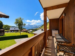 A wooden balcony with a view of a green landscape and mountains in the background.