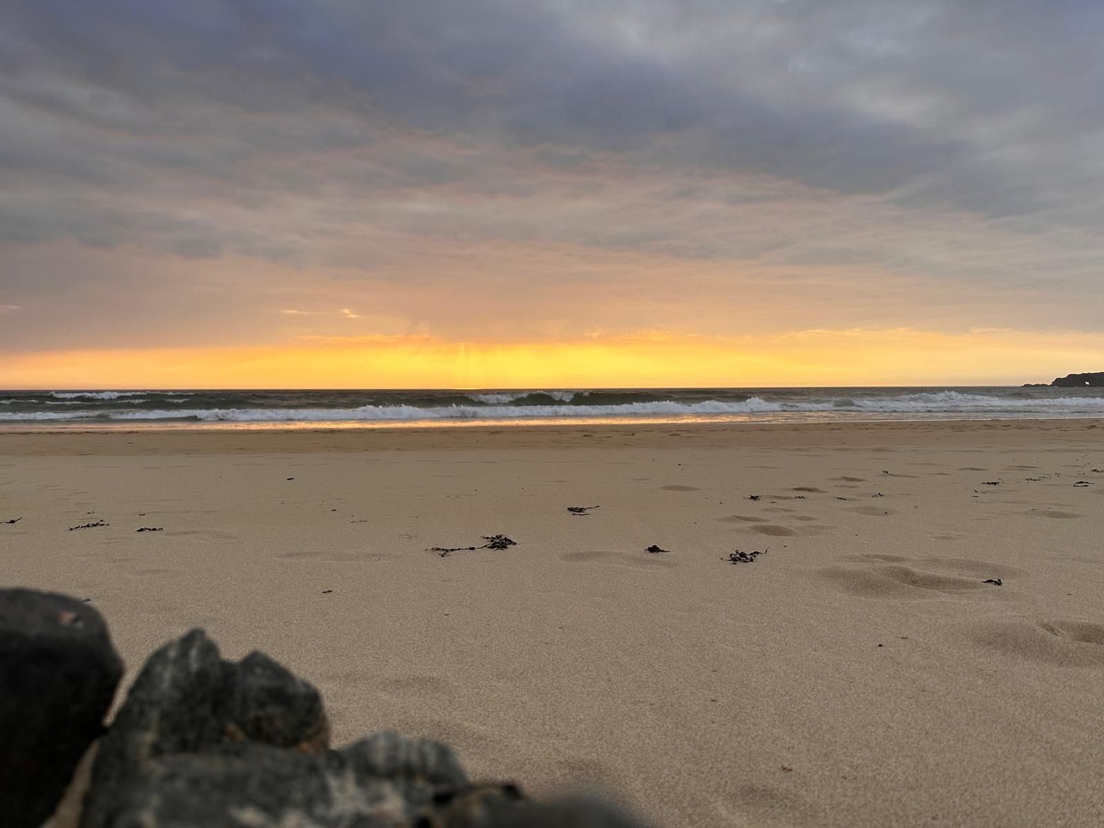 A beach with a sunset, waves, and footprints.