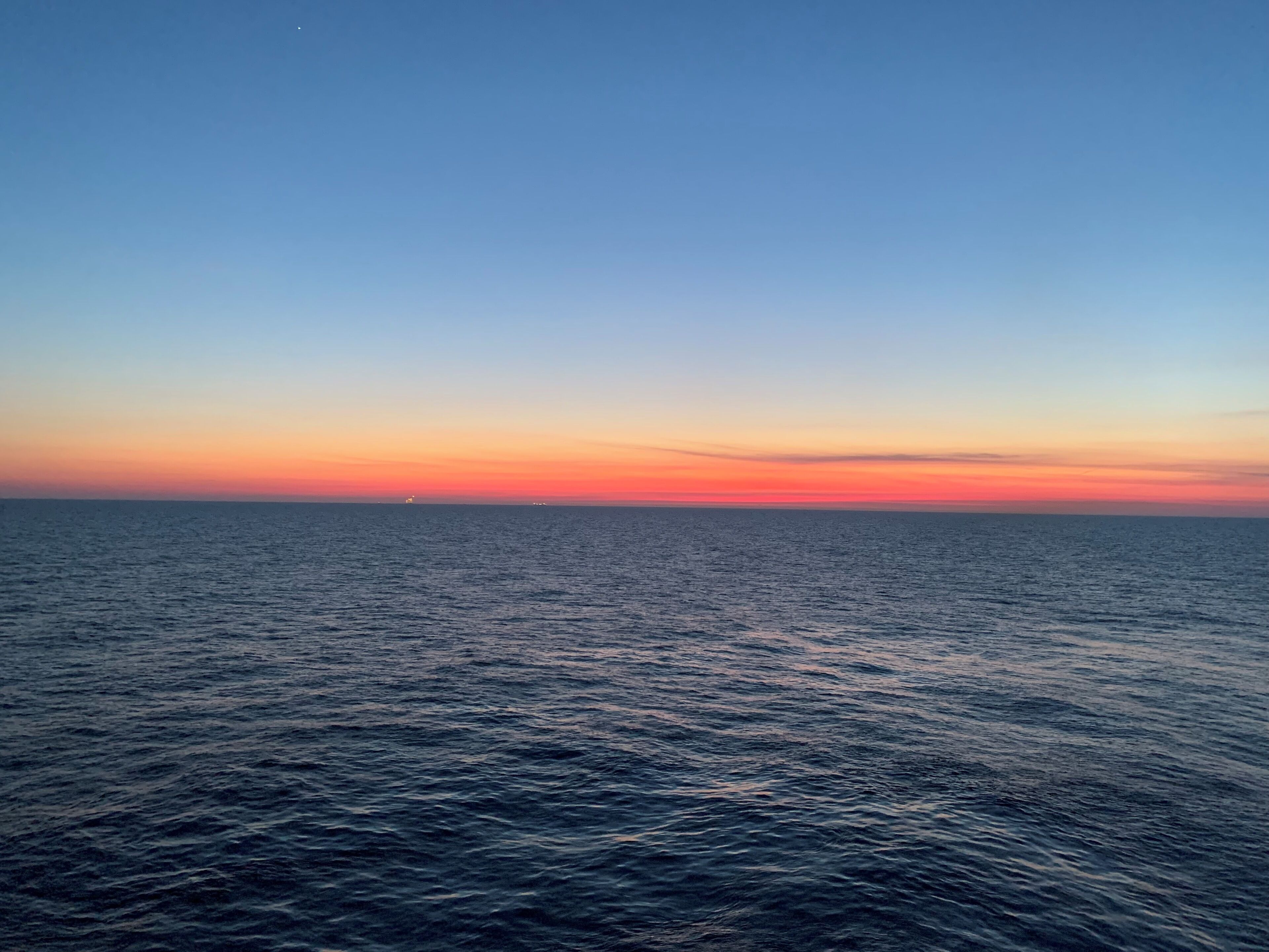 A calm sea at sunset with a clear sky.