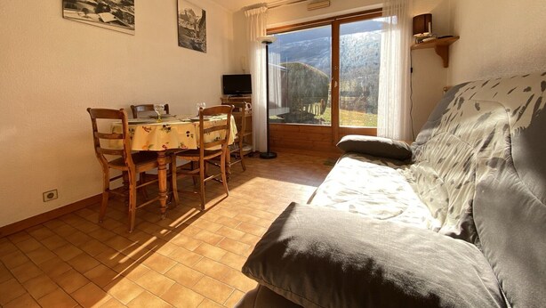 A cozy room with a dining table, chairs, a sofa, and a large window offering a scenic view.