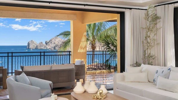 Ein geräumiger Balkon mit Blick auf das Meer und felsige Klippen, ausgestattet mit einer Couch, Stühlen und einem Couchtisch.