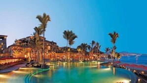 Ein Resort mit großem Pool, Palmen und Blick auf das Meer im Abendrot.
