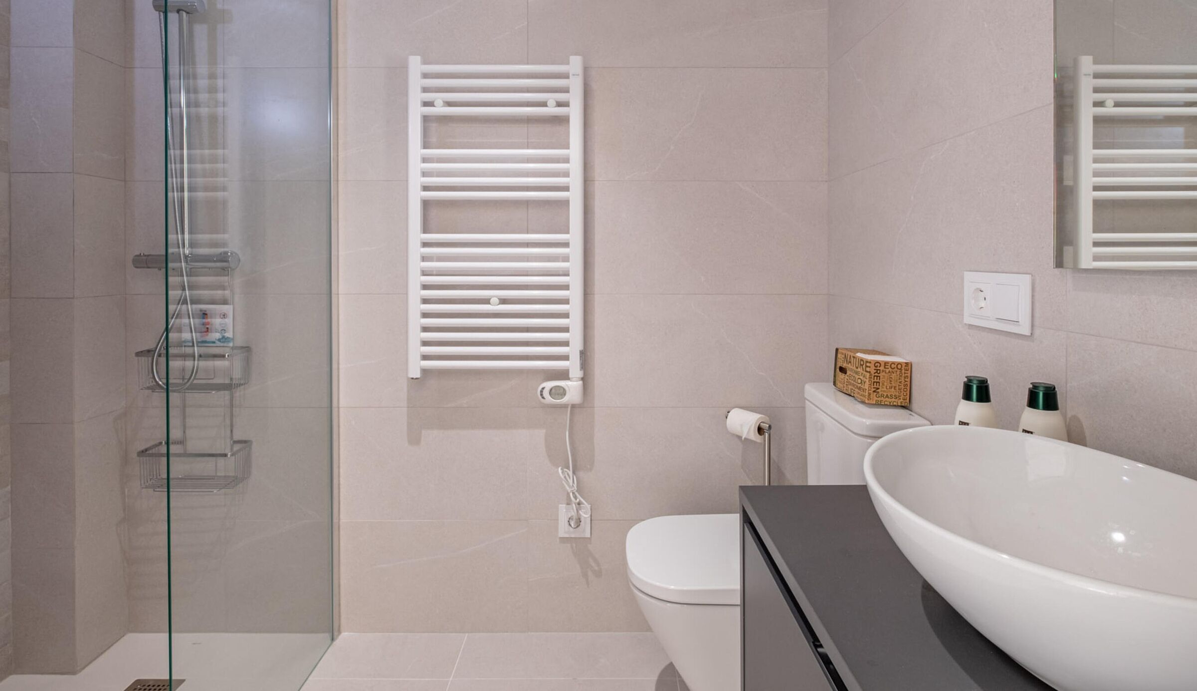 Ein modernes Badezimmer mit einer Duschkabine aus Glas, einer weißen Toilette, einem weißen Waschbecken mit großem Becken und einem an der Wand montierten Handtuchhalter.