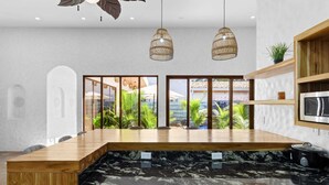 A modern kitchen with a wooden island, black marble countertop, and hanging wicker pendant lights. - Modern Home with Chic Bohemian Style and “Zen” Outdoor Oasis with Swimming Pool and Tiki-Style Dining Space (Potrero)