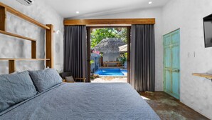 A bedroom with a large bed, a wooden headboard, a TV, and a view of an outdoor pool area. - Modern Home with Chic Bohemian Style and “Zen” Outdoor Oasis with Swimming Pool and Tiki-Style Dining Space (Potrero)