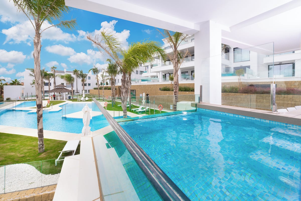 A modern hotel with a large indoor swimming pool, palm trees, and a clear blue sky.