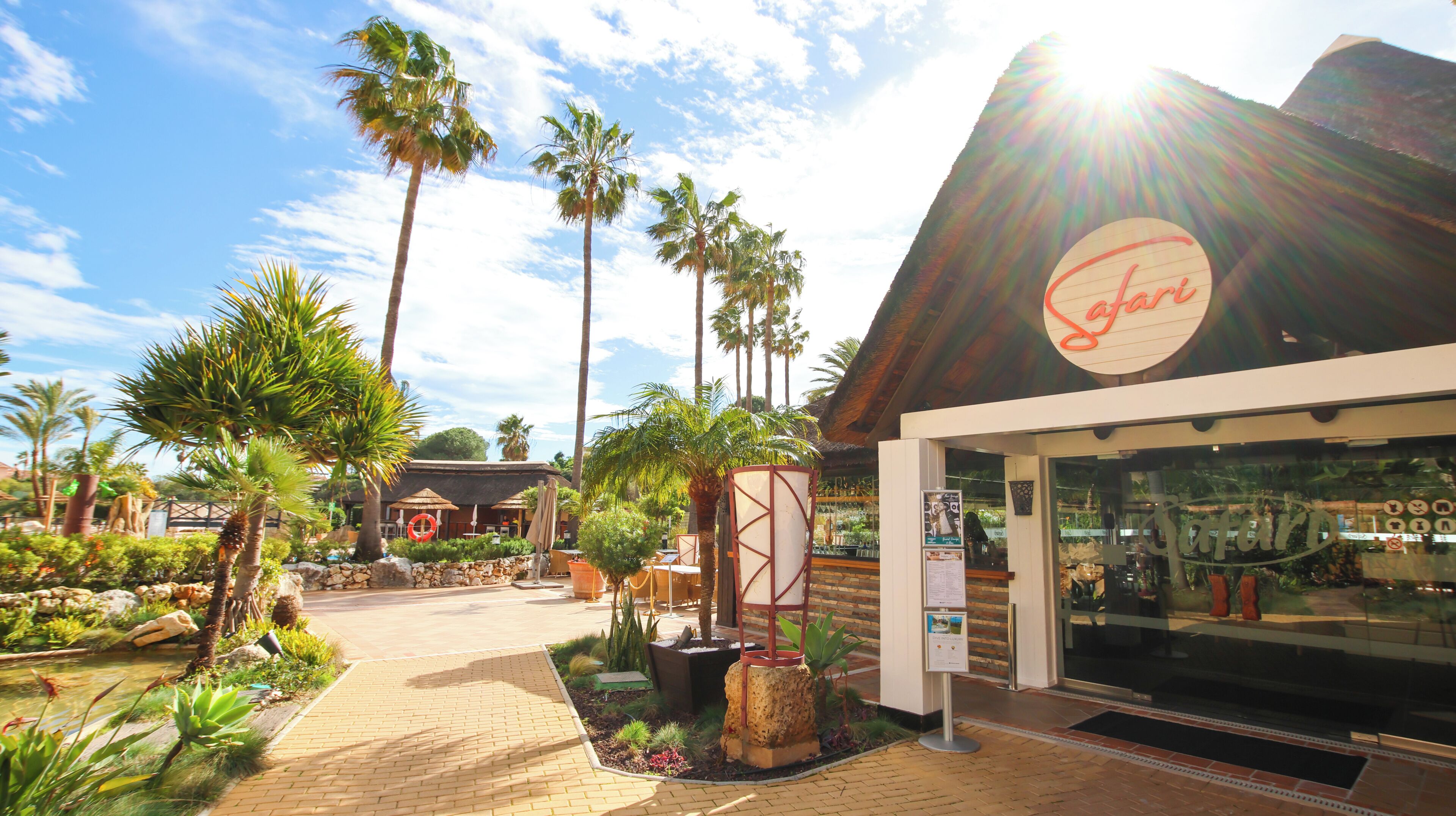 A restaurant with a tropical theme, palm trees, and a brick pathway.