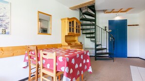 A dining area with a table covered in a red tablecloth with white patterns, wooden chairs, a wooden cabinet, a mirror on the wall, and a blue door with a spiral staircase leading to an upper level. - Sunny duplex for 6 in Avoriaz (Avoriaz)