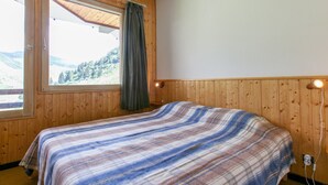 A room with wooden walls, a bed with a striped blanket, a window with a view of a forest, and a wall-mounted lamp. - Sunny duplex for 6 in Avoriaz (Avoriaz)