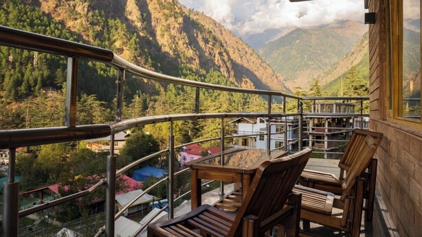 Un balcone con vista su un paesaggio montuoso, sedie di legno e un parapetto.