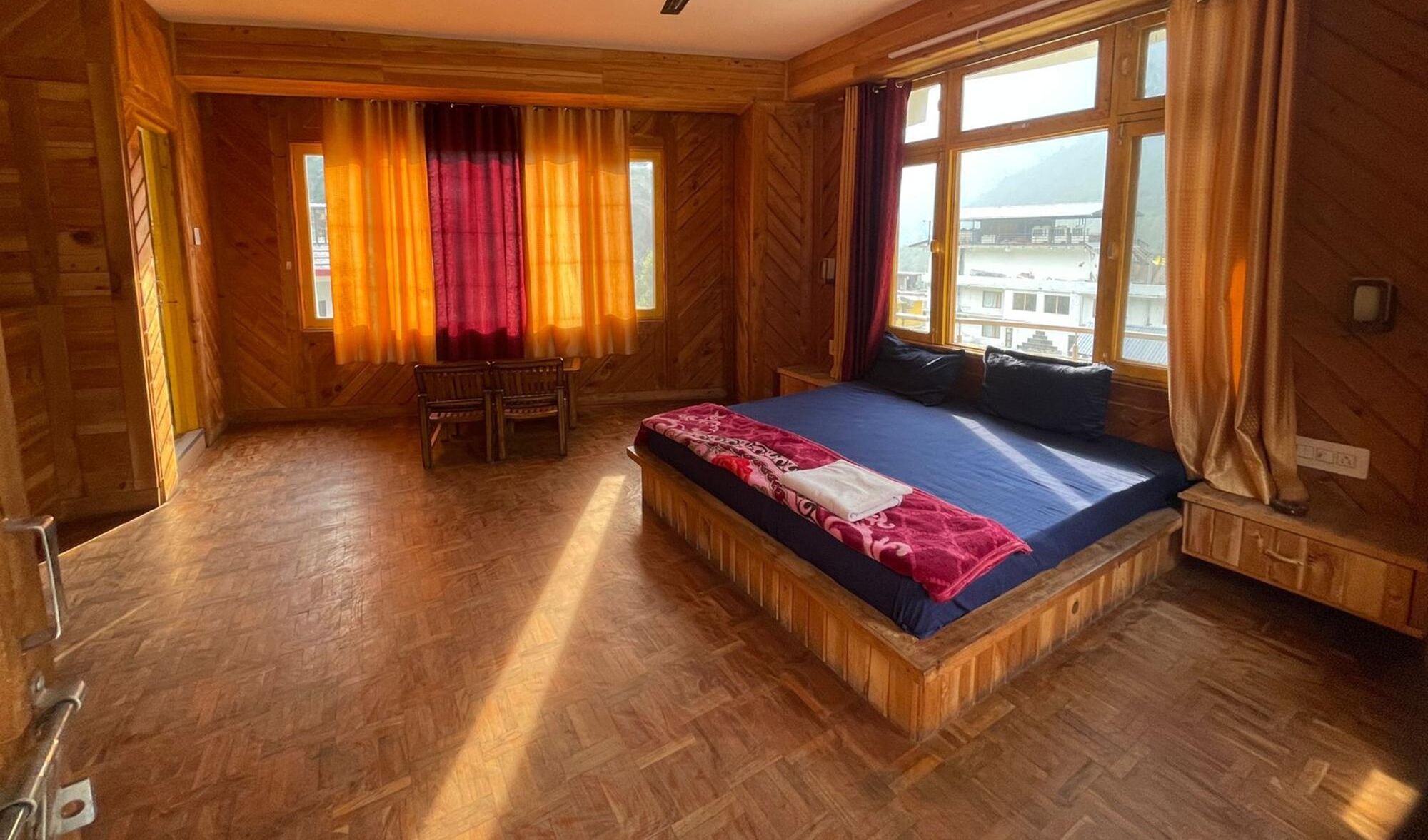 A wooden room with a large bed, a bench, and a window with curtains.