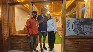 Una baita di legno con ingresso tramite una porta in vetro, un piccolo ambiente interno con tappeto verde e una parete decorata con diversi disegni e una insegna.