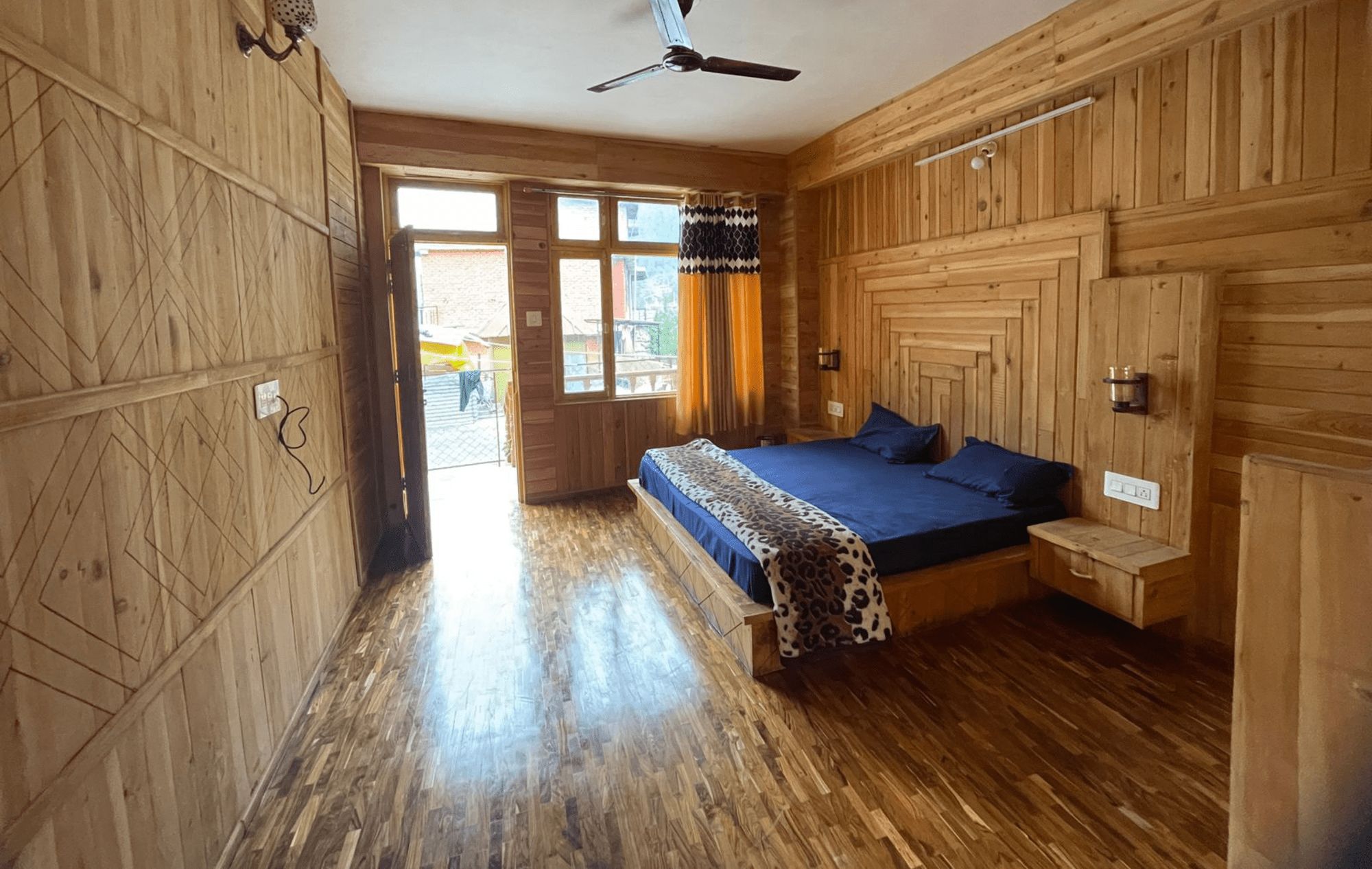 A wooden room with a bed, a ceiling fan, and a window.