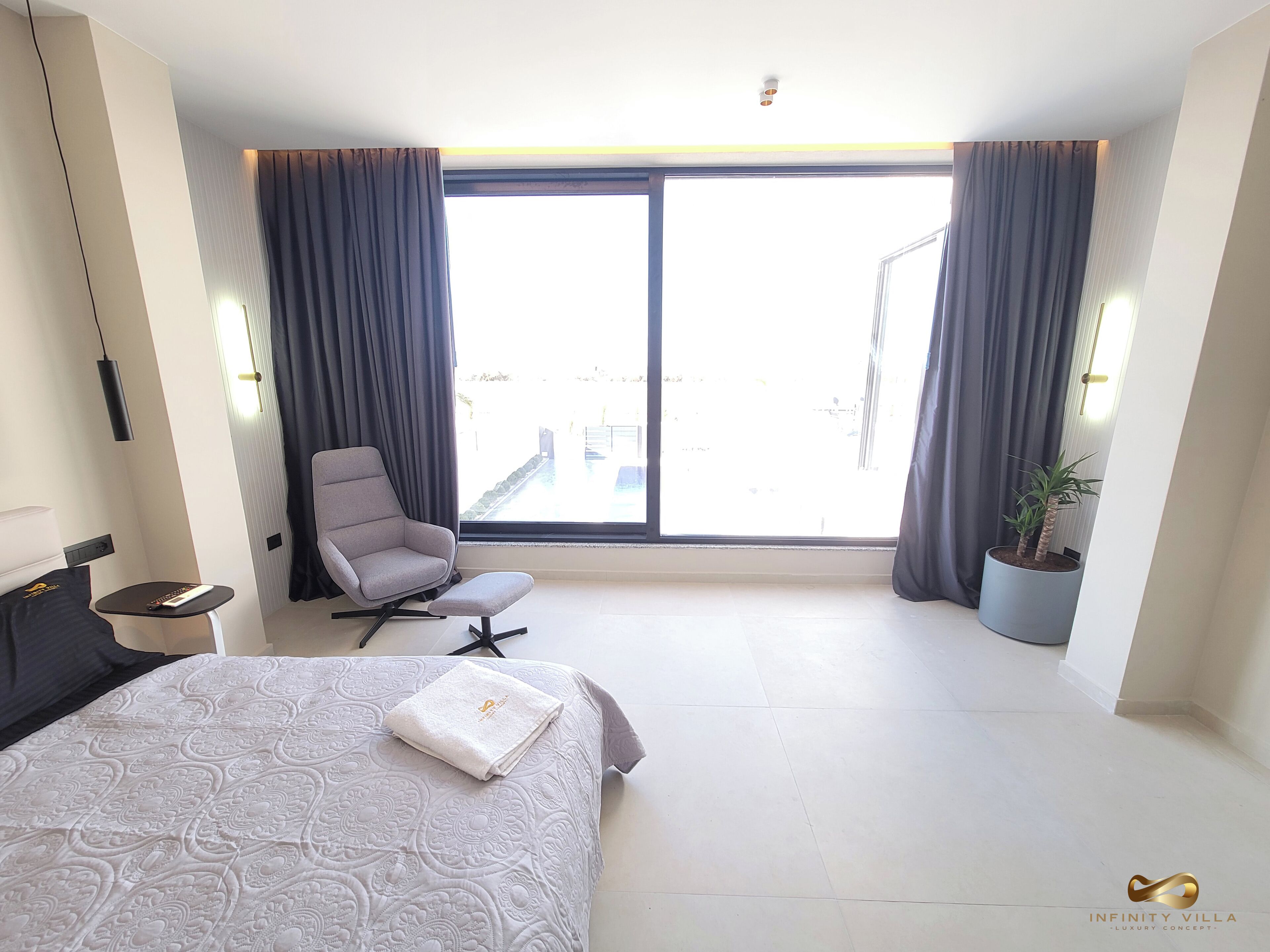 Ein modernes Hotelzimmer mit einem großen Bett, einem Sessel, einem kleinen Tisch und einer Topfpflanze.