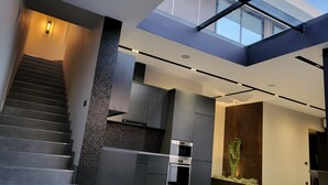 A modern interior with a staircase, a kitchen with stainless steel appliances, and a living area with a glass ceiling. - La Mirage Group Villas (Sukth)