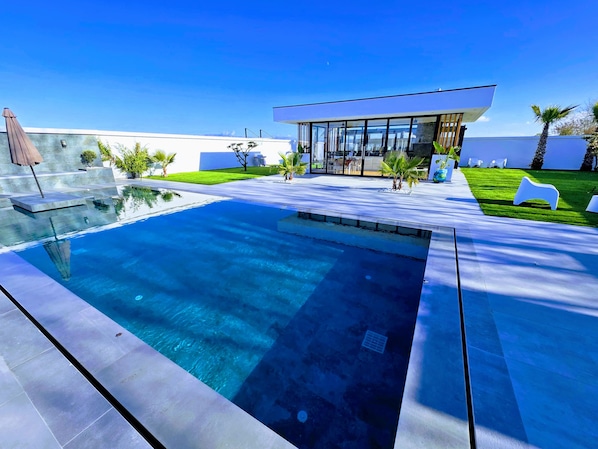 A modern outdoor pool area with a clear blue pool, a glass-enclosed structure, and well-maintained grass. - La Mirage Group Villas (Sukth)