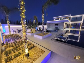A modern villa with a pool, outdoor seating, and illuminated trees. - La Mirage Group Villas (Sukth)