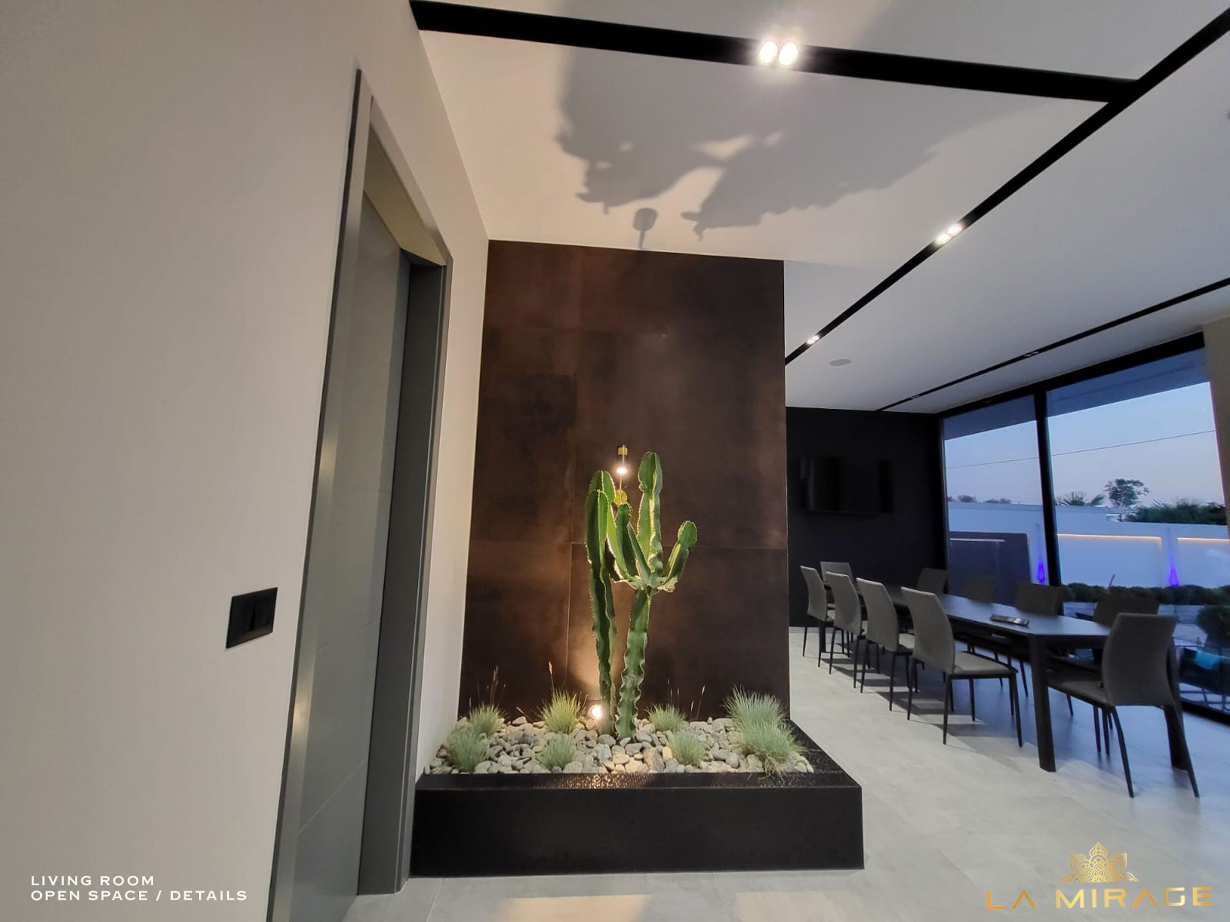 A modern living room with a large cactus centerpiece, a dining area with chairs, and a view of the outside.