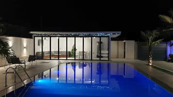 Piscina com cobertura de vidro e cadeiras, cercada por um edifício com um pinheiro de Natal e uma garagem.