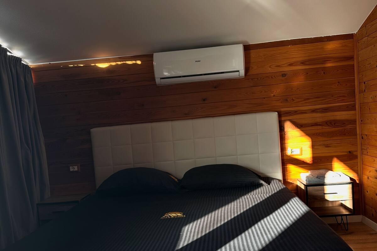 Une chambre à coucher comprenant un lit, une table de chevet, une lampe et un appareil de climatisation.