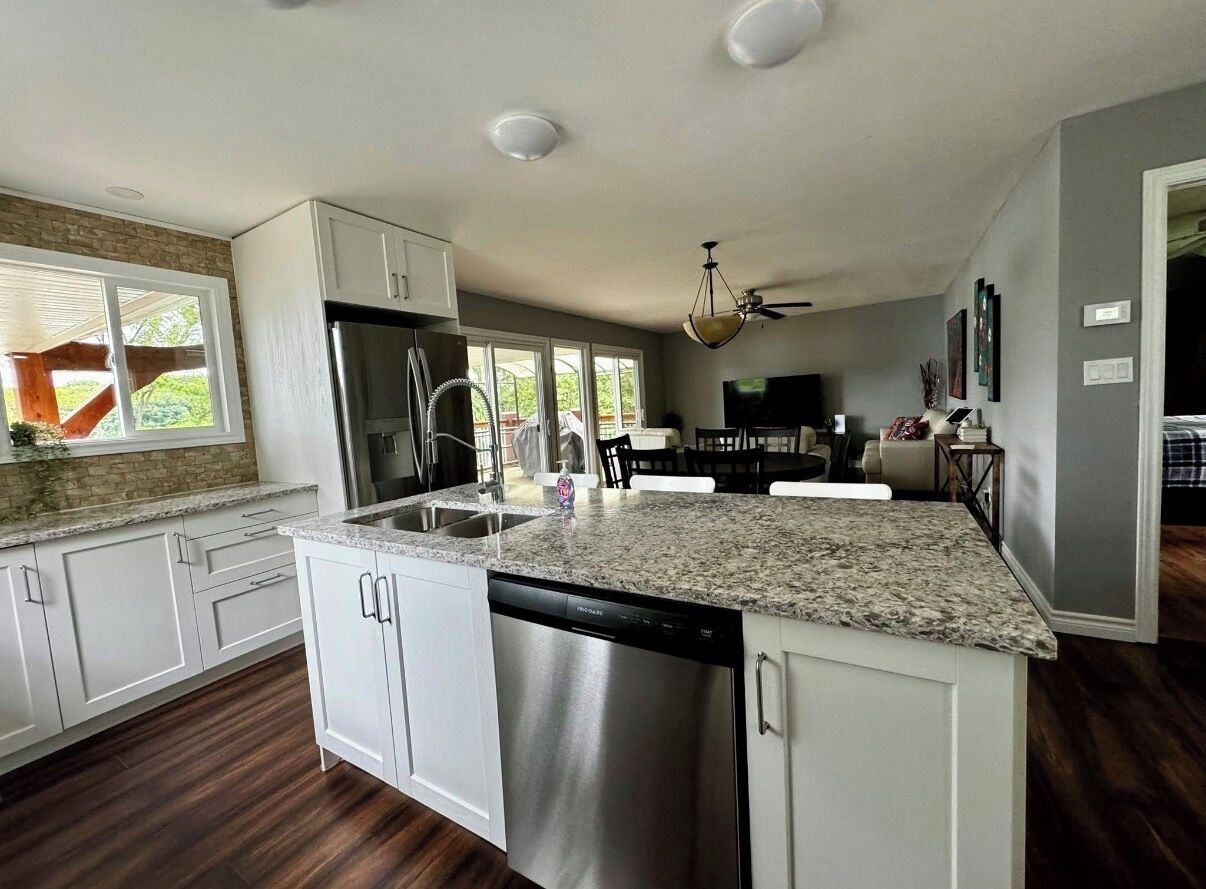A modern kitchen with white cabinetry, a stainless steel dishwasher, and a granite countertop.