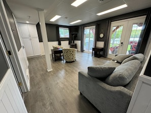 A spacious living area with a grey sofa, a patterned armchair, a small table, and a television.