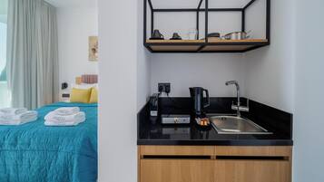 Una habitación de hotel con cama, kitchenette, cafetera y lavamanos.