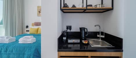A hotel room with a bed, a kitchenette, a coffee maker, and a sink.