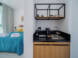 Una habitación de hotel con cama, kitchenette, cafetera y lavamanos.