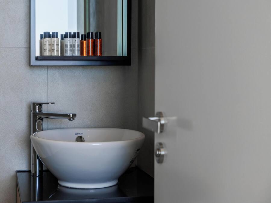 Un baño con un lavamanos blanco, grifo cromado y un espejo encima.
