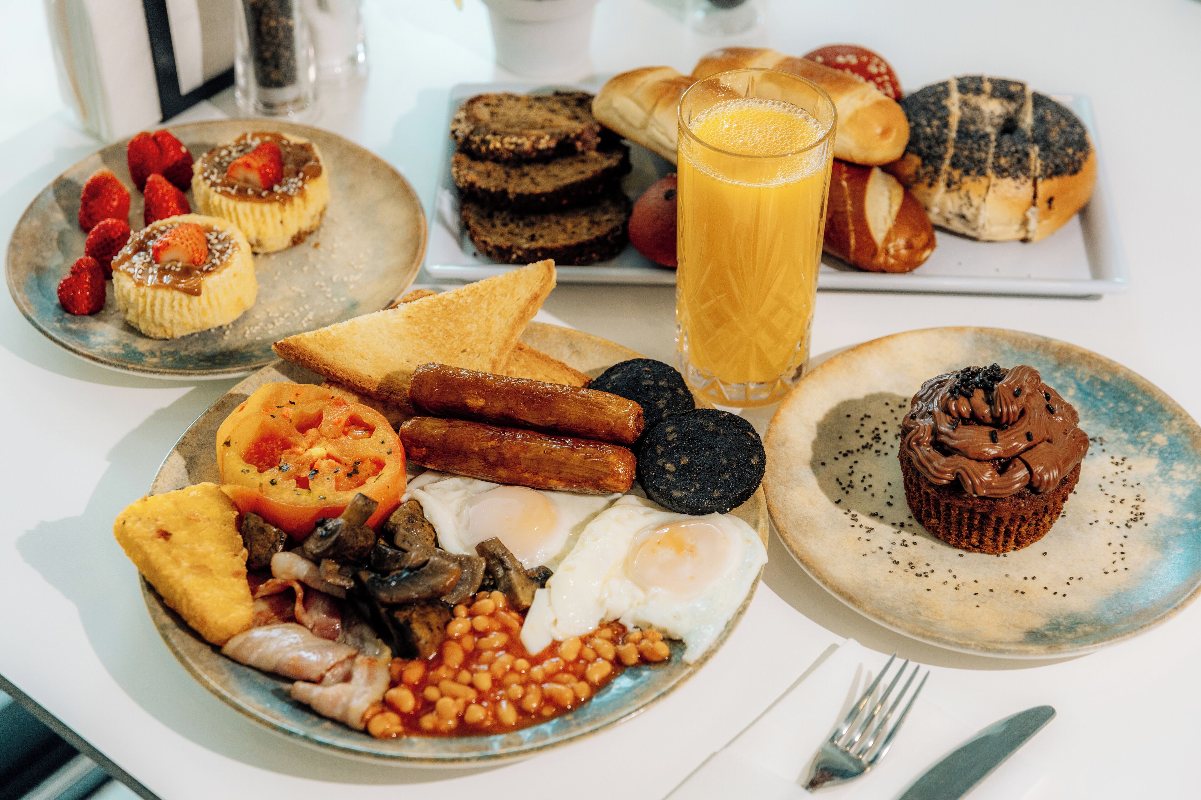 Una abundante mesa de desayuno con tostadas, salchichas, huevos, frijoles y un muffin.