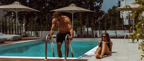 A swimming pool with metal ladders, surrounded by lounge chairs and umbrellas.