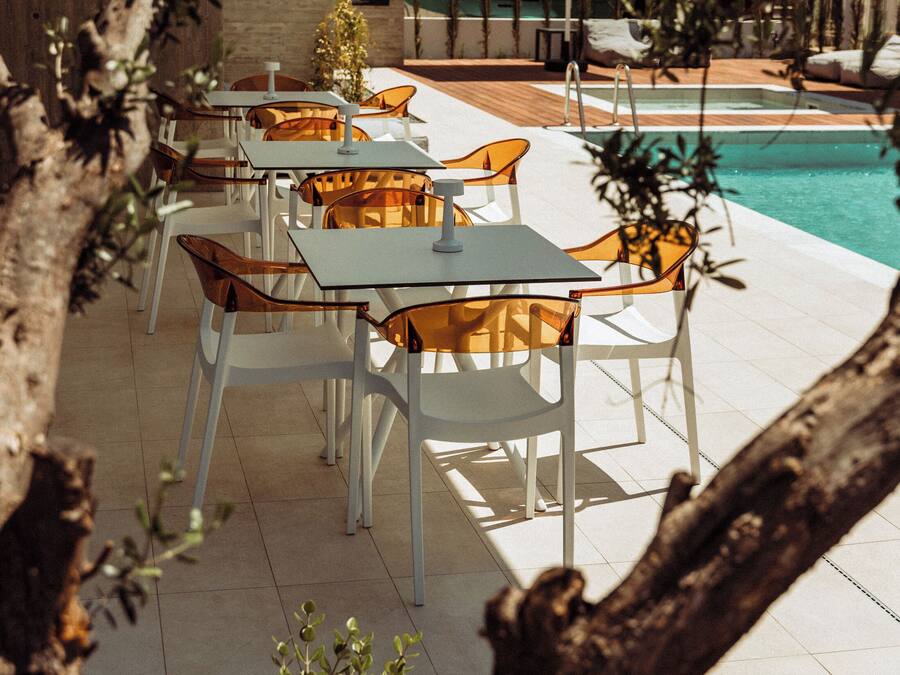 Un espacio al aire libre con mesas, sillas, una piscina y una terraza de madera.