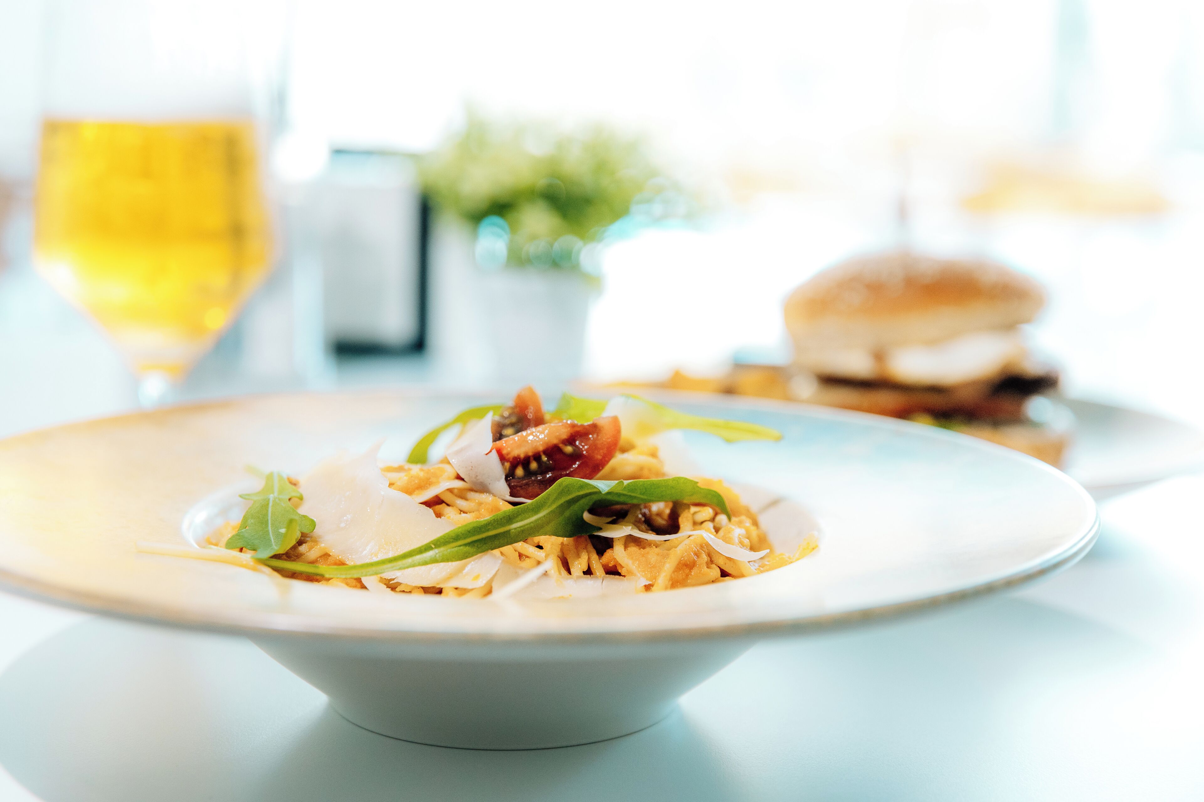 A plate of food with a glass of wine and a burger in the background.