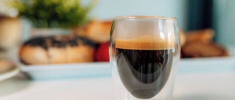 Una taza de café transparente con espuma sobre una superficie blanca.