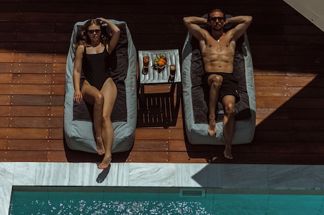 Two lounge chairs on a wooden deck with a pool below.