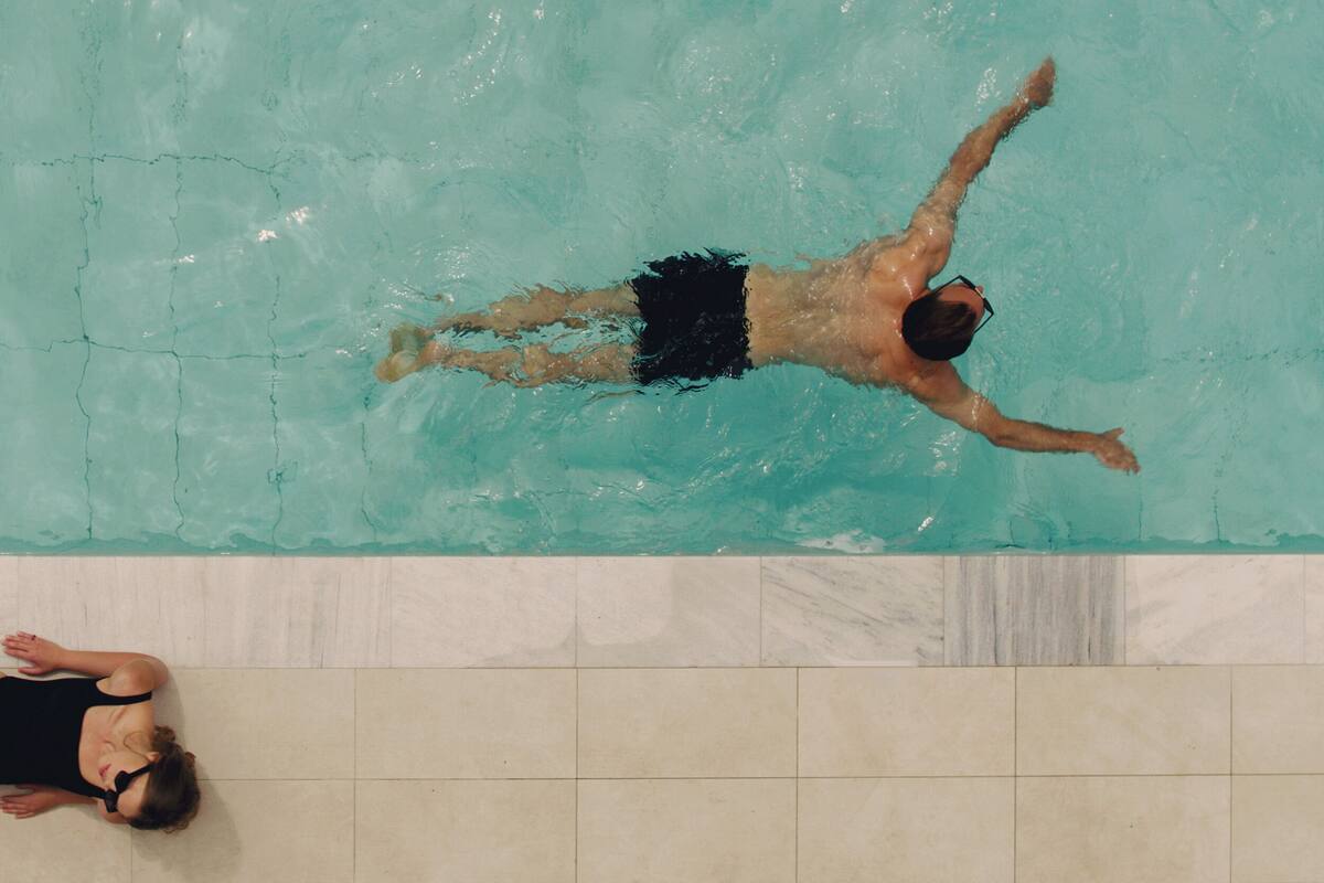 Una piscina con dos personas, una nadando y otra recostada al borde.