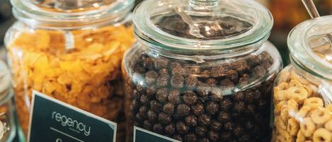 Exposição de diversos produtos de cereais em potes de vidro com etiquetas, incluindo 'regency' e 'cereal'.