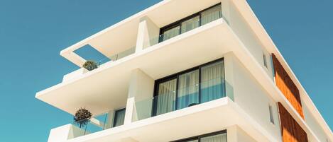 A modern multi-story building with balconies, large windows, and a clear blue sky.