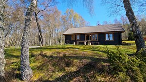 A cabin with a tiled roof, wooden exterior, and a porch with benches. - Balbeag Cottage - Pet friendly Log Cabin (Insh)