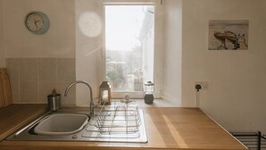 A kitchen with a sink, a clock, a window, and a painting on the wall.
