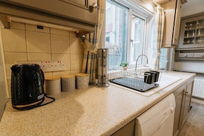 A kitchen with a countertop, a kettle, a coffee maker, a sink, and a window with curtains.