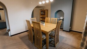 A dining area with a wooden table and chairs, a bookshelf, and a decorative archway. - Cumbria House: Stunning Views, 3 Bedrooms & Garden (Fletchertown)