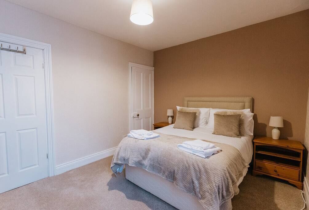 Een slaapkamer met een bed, twee nachtkastjes, een deur en een lamp.