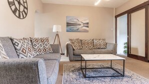A living room with two grey sofas, patterned cushions, a coffee table, a floor lamp, and a painting on the wall. - Cumbria House: Stunning Views, 3 Bedrooms & Garden (Fletchertown)